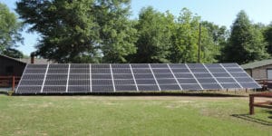 A large, residential ground-mounted solar panel system in a yard with trees in the background.