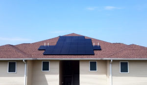 A solar panel system installed on a red shingle roof of a shingle-family home.