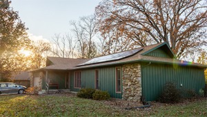 A single-family home with stone siding has a newly installed solar panel system on the roof.