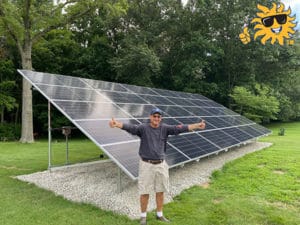 A man stands in front of a newly installed ground-mounted solar panel on his property holding two thumbs up.