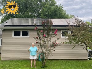 A woman stands outside of her home with newly installed solar panels on the roof giving two thumbs up.