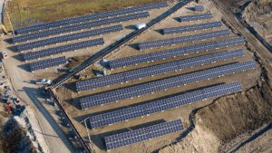 An aerial image of an industrial facility with rows of ground-mounted solar panels.