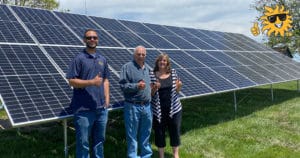 A family gives the thumbs up in front of a ground-mounted solar panel system installed on their land.