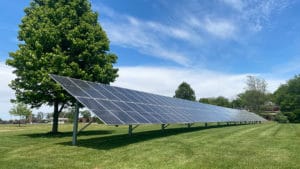 A large solar panel array installed in a field with trees in the background.