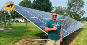 A homeowner in a green shirt stands in front of newly installed ground-mounted solar panels giving the thumbs up.