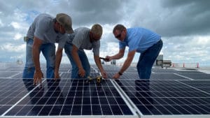 Three technicians work on installing a roof-mounted solar panel system.