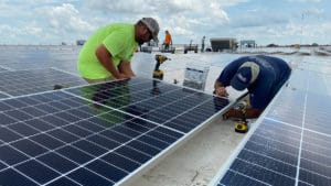 Two technicians work on installing solar panels on the roof of a commercial building.