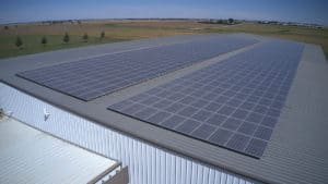 A large warehouse that with two rows of commercial solar panels installed on the roof.