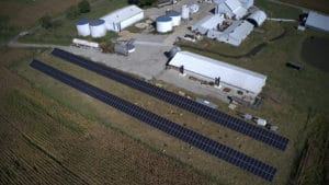 An aerial image shows two rows of ground-mounted solar panels outside of an industrial site.