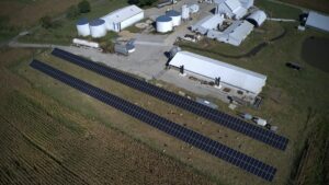 An aerial image of an industrial facility with two large rows of ground-mounted solar panels on the property.