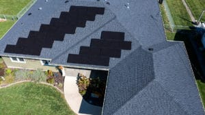 An aerial image of a home with a gray shingle roof that has two sections of solar panels.