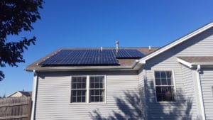 A roof-mounted solar panel system on a home with gray vinyl siding.