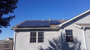 A small home with white siding has solar panels installed on the roof.