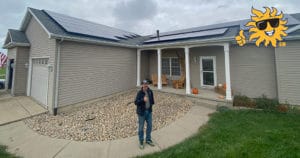 A man gives the thumbs up outside of his home with newly installed roof-mounted solar panels.